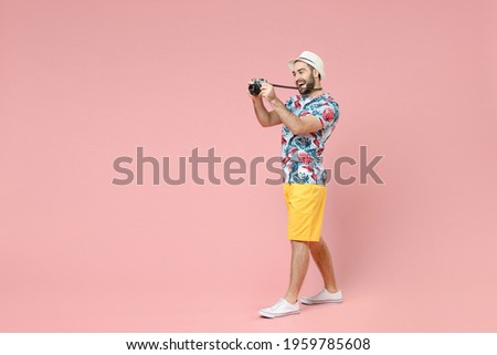 Full length side view of funny traveler tourist man in summer clothes hat taking pictures on vintage photo camera isolated on pink background. Passenger travel on weekends. Air flight journey concept