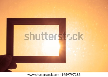 male Hand holding a wooden frame on sunrise sky background. Care, safety, memory or painting concept.