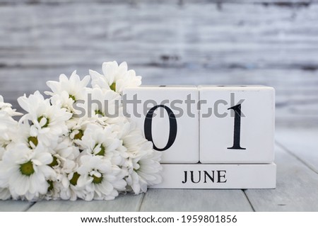 White wood calendar blocks with the date June 1st and white daisies. Selective focus with blurred background. 
