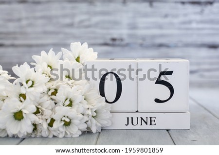 White wood calendar blocks with the date June 5th and white daisies. Selective focus with blurred background. 