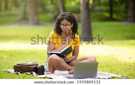 Thoughtful female student with laptop and notebook studying online at park, panorama