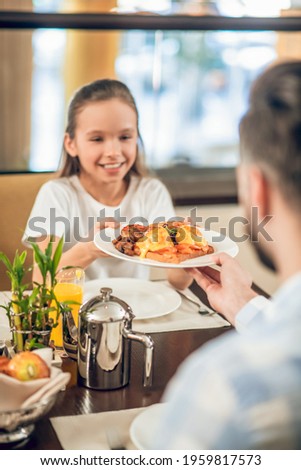Pretty teen girl taking a plate with food from her dads hands