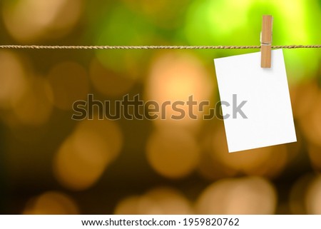 Blank sheets of paper hang on a rope with clothespin on bokeh background.