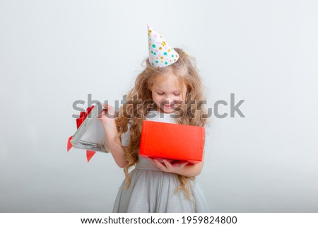 a happy little girl in a festive hat holds a gift on a white background