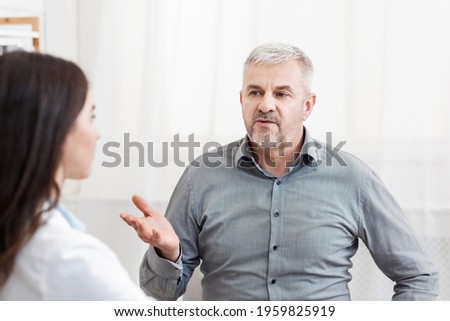 Doctors help, visit to therapist, consultation, health problems, medical support, services and care. Elderly patient complains to young woman in protective mask and white coat in modern office