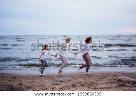 A beautiful mother with her daughters holding hands are running merrily along the beach by the sea. Happy family on vacation. White Nights  