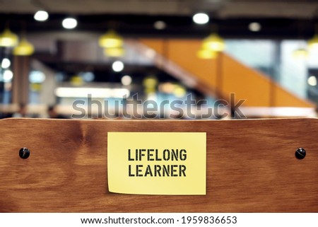 Wooden chair back with note sticking LIFELONG LEARNER, refers to those who gain knowledge by learning new skills throughout life- continue education for personal development or fulfillment Royalty-Free Stock Photo #1959836653