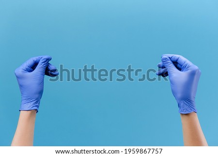 Close up of male hands in medical protective latex gloves rubbing fingers showing cash gesture asking for money, isolated on blue studio wall with copy space for advertisement. Body language concept