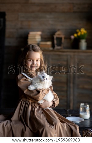 Portrait of a girl in a vintage dress. A girl with long hair in a brown dress with a white collar. The girl is holding a white kitten in her arms. Image with selective focus.