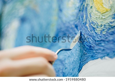 the hand of a European artist holds a mastekhin smeared in oil paint and draws a picture. Van Gogh's replica Starry night. blurred background. Close-up. Royalty-Free Stock Photo #1959880480