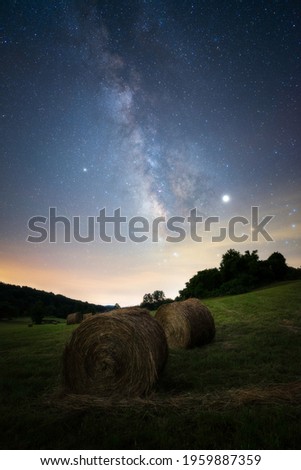 A beautiful nightscape of hay bales  on a field with the Milky Way glowing in the night sky.