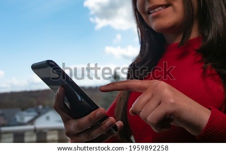 Woman stands at the window and types on their cell phone. Background with blue sky and white clouds.