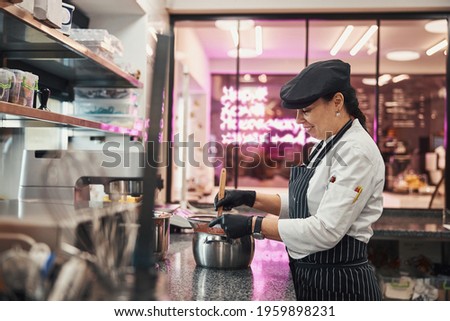 Pleased pastry chef stirring her concoction in metal pan Royalty-Free Stock Photo #1959898231