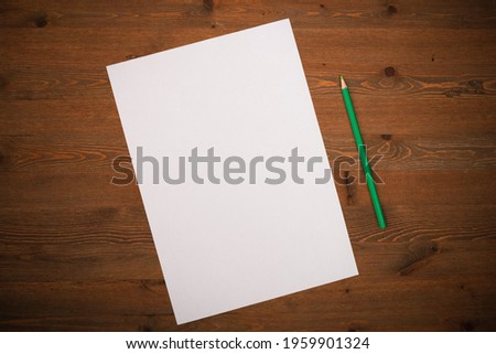 A blank white sheet and pencil for drawing on a wooden background with space for copying and lettering. Layout, mockup free space.