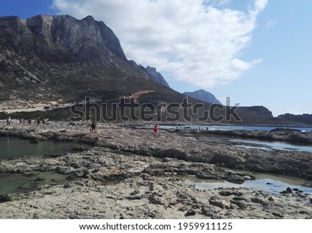 Unidentified people sunbathing and strolling along the beach in Balos Lagoon on Crete, Greece. Beautiful view of mountain next to beach against blue sky