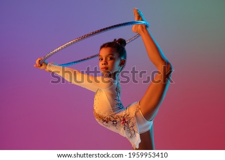 Energy, dynamic. African-american rhythmic gymnast, pretty girl practicing on gradient studio background in neon light. Concept of human emotions, sport, action and motion, youth, sales, ad.