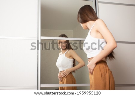 Anorexia in teenagers, a teenage girl looks in the mirror and sees herself fat, a disease, a disorder of the psyche and eating behavior Royalty-Free Stock Photo #1959955120