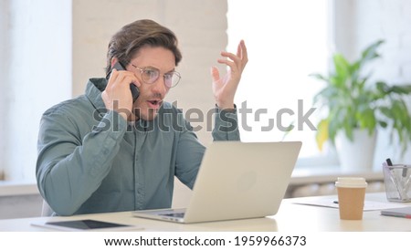 Angry Man with Laptop Talking on Smartphone