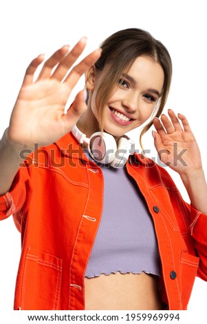 joyful woman in orange shirt and wireless headphones gesturing isolated on white