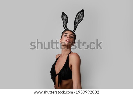 Portrait of young woman with bunny ears posing over grey background.