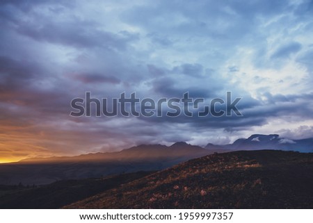 Atmospheric landscape with silhouettes of mountains with pink flowers on hill on background of dawn sky with long orange sun ray on mountain. Vivid scenery with sunset or sunrise of illuminating color