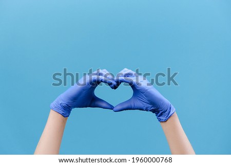 Close up of male hands in medical protection gloves making heart symbol as a way to show thank gratitude to doctors and nurses for help in fight against disease, isolated on blue background. COVID 19 Royalty-Free Stock Photo #1960000768