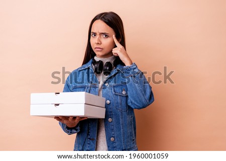 Young mixed race woman holding a pizza isolated pointing temple with finger, thinking, focused on a task.