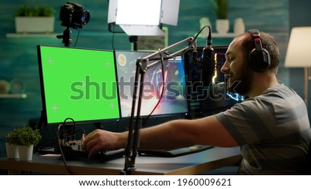 Professional cyber streamer playing online videogames on professional powerful computer with green screen mock up, chroma key display. Gamer playing space shooter game with isolated desktop streaming