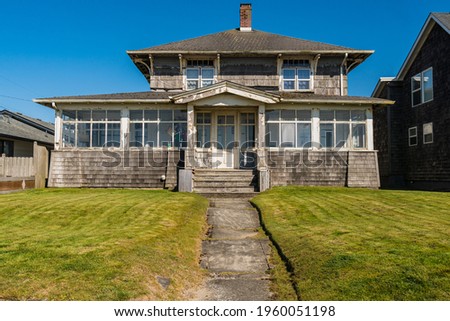 Old weathered and worn coastal beach front house with cedar shake shingles and white windows. Royalty-Free Stock Photo #1960051198