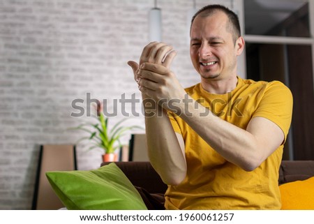 Unhappy middle aged man holding his painful wrist caused by prolonged work on the computer, laptop. Carpal tunnel syndrome, arthritis, neurological disease concept. Numbness of the hand