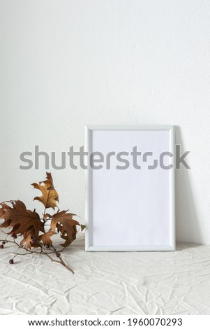 Home decor mocap, empty picture frame near white painted concrete wall, branches with dry leaves