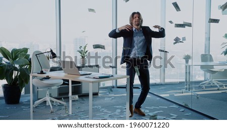 Emotional young rich businessman dance in money rain celebrating successful start-up launch project inside corporate office workplace.