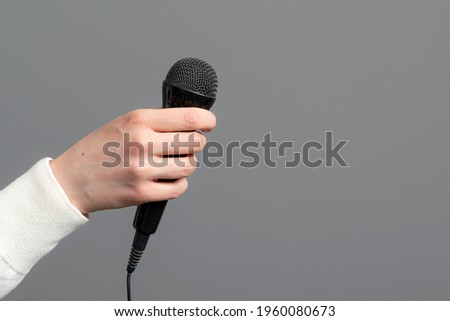female hand with microphone on gray background, close-up
