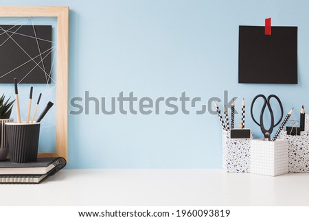 White table - workspace, with books and office supplies against blue wall background. Royalty-Free Stock Photo #1960093819