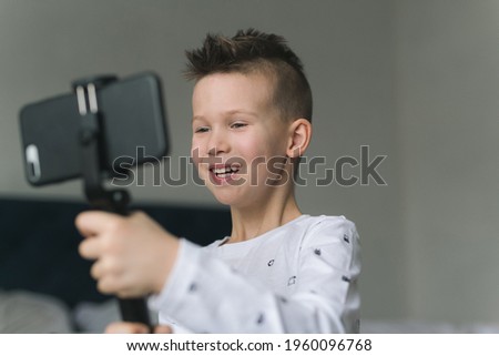 A seven-year-old boy, in light-colored clothes, holds a phone in his hands, takes pictures, conducts video chat with friends, communicates with people in quarantine. Modern technologies