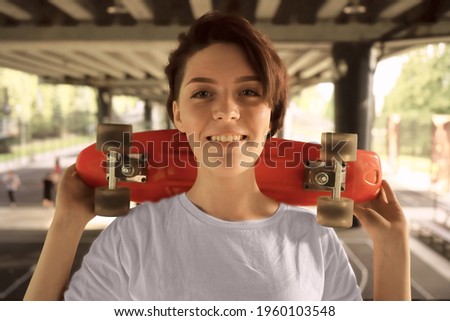 Portrait of a young happy beautiful woman with short hair. hipster girl in white shirt holding skateboard on shoulder. bridge background. Copy space. Lifestyle and street style concept.
