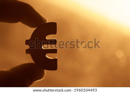 male hand hold the Euro sign, symbol. sunny yellow sky on background. sun rays. euro symbol of money.  idea of Euro Union