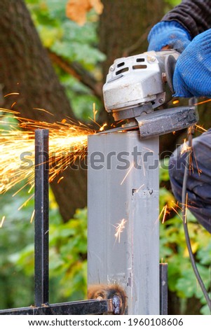 The hands of a worker professionally wield an angle grinder when cutting a metal fence and deburring with fly of hot sparks. Vertical image, selective focus, copy space.