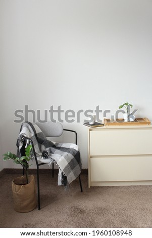 Stylish composition of bedroom interior with wooden commode and comfortable armchair. Cozy home decor.