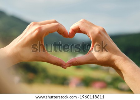 Heart shape from the hands of a girl on a background of nature. Hand gestures. Beautiful hands with copy space. Love for nature. Appreciation gratitude and love concept