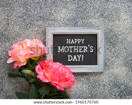 Happy Mother's Day greeting card. Peony flowers and blackboard with greeting text on textured stone background. Monochrome look, black and grey colors.