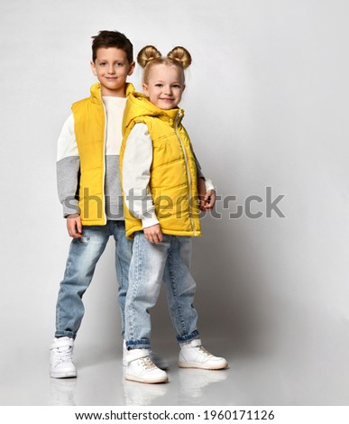 teenage boy and girl posing against a light background, children are dressed in yellow puffy sleeveless zipper vests and jeans. urban teen fashion Royalty-Free Stock Photo #1960171126