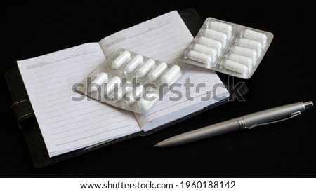 A prescription notebook, a ballpoint pen and white capsules in a blister lie on a dark background. Close-up