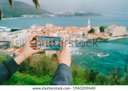 Girl's hands hold a smartphone with a photo of buildings on the background of the city of Budva