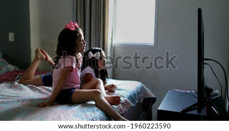 Children watching movie at home, girls lie in bed hypnotized by screen