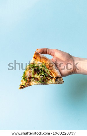Woman is holding a slice of pizza with fresh arugula on blue studio background, close up, studio shot