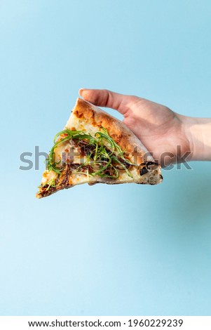 Woman is holding a slice of pizza with fresh arugula on blue studio background, close up, studio shot