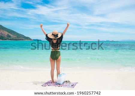 Full body Asian woman wearing hat See-through and green bikini outstretched arm on beach with sea and sky background in the daytime. Concept of long weekend holidays and travel. Copy space for text.