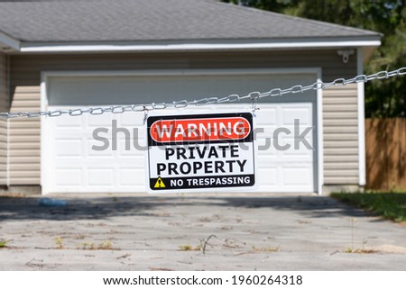 A private property no trespassing sign hangs from a chain across a driveway in front of a garage of a suburban house