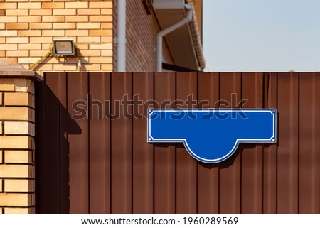 A blue address sign on the fence of a private house.
